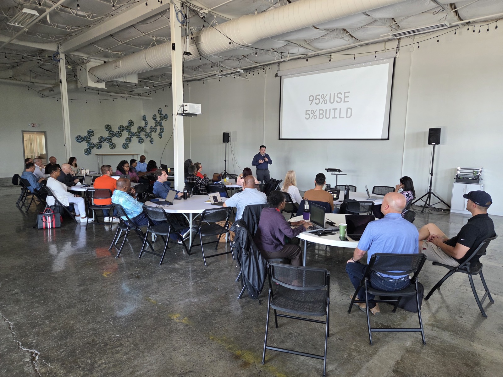 Facilitator presenting to a seated room, “95% use, 5% build” on screen